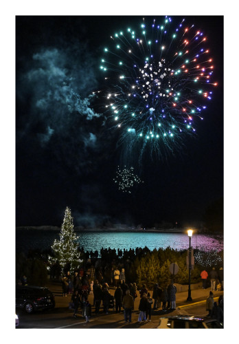 Fireworks over a holiday tree with a bunch of people standing around