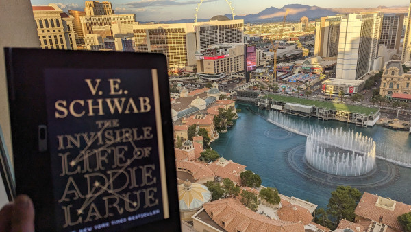 Tablet showing the cover of ebook The Invisible Life of Addie LaRue by V.E. Schwab. In the background is a view from a room in the Bellagio Las Vegas: the famous Bellagio fountains, the Las Vegas Strip, Paris Las Vegas, Horseshoe Casino, The Cromwell, Harrah's, The Venetian, Encore, and Caesars Palace.