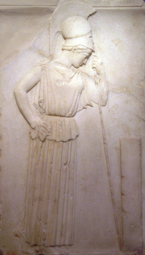 The goddess Athena is depicted standing up. She wears an Attic peplos and a Corinthian herlmet; she rests her head on her spear. Athena’s head is bowed as she contemplates a rectangular stele. (adapted from Wikimedia commons).