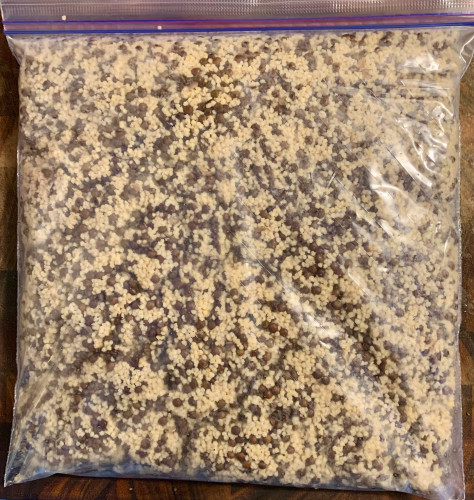 A plastic bag lying flat and filled with small tan grain (millet) and small black lentils (beluga).