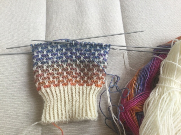 Chaussette tricotée à 5 aiguilles avec une pelote crème et une pelote multicolore.
Sock on needles with two yarns: a cream one and a multicolored one (orange, purple, blue, pink and green)