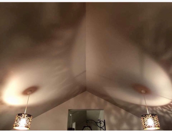 Photo depicts a pitched ceiling with decorative hanging lights that cast a pattern that resembles naked breasts. 