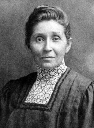 Black and white photograph of Dr. Susan La Flesche Picotte. She looks straight at the viewer with a calm expression on her face. Her hair is up and back in a bun and she wears a dress with a high lace collar. 