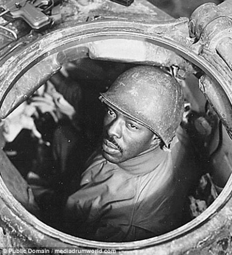 Black and white image of World War II black soldier sitting in an armored tank and looking at camera.