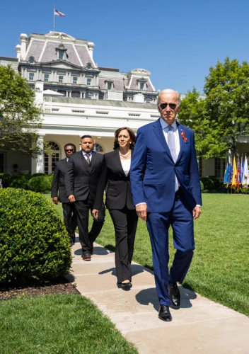 Biden. Kamala Harris, and two gentlemen walking in a formation with confidence down a path from a white building towards the camera.