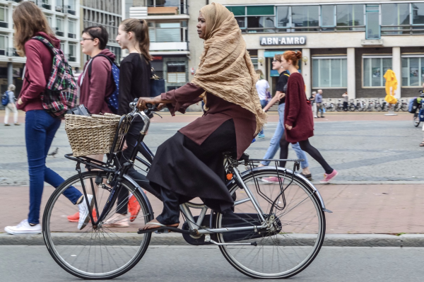 A young woman dressed in a burka rides an upright Dutch-style bicycle in a public square in the medieval center of Groningen.