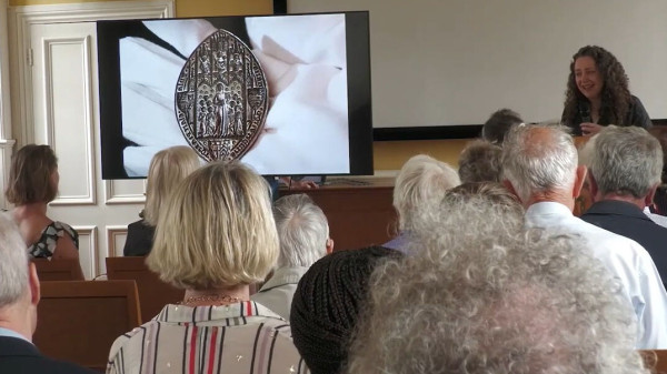 Photo of the lecture: Dr Jackie Tasioulas explains the significance of the seal, with an image of the silver matrix in the palm of a gloved hand.