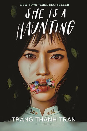 Cover of the book “She Is A Haunting”, depicting a close up face of a dark haired Vietnamese woman, tears streaking from her right eye, half open month having hydrangea flowers sprout and spread from it 