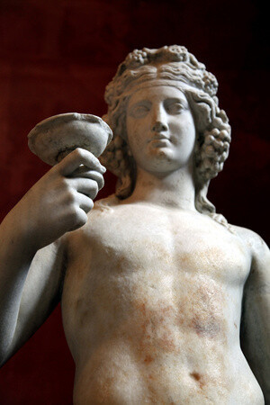 Roman marble sculpture of Dionysos, God of Wine and patron of wine-making, created after a Greek model of the 4th century BCE. The god, crowned with lush clusters of grapes, holds up a cup as if to toast to the onlooker.