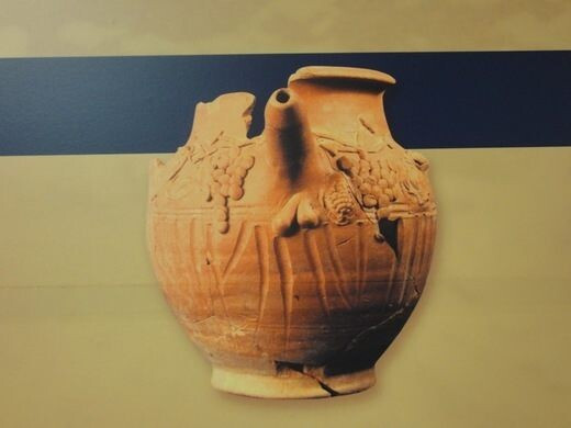 A terracotta wine jug with grape cluster decorations an erect phallus for a nozzle. Testicles are fashioned below it.