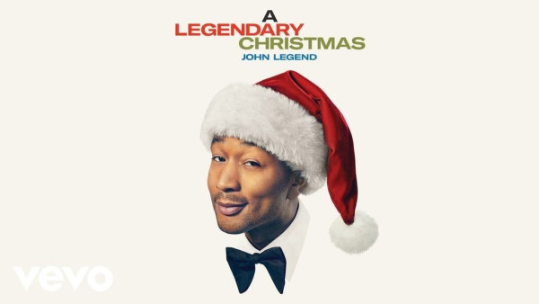 John Legend donning an oversized bowtie, a Santa hat, and a roguish smirk ... only visible from the collar up ... on a white background.