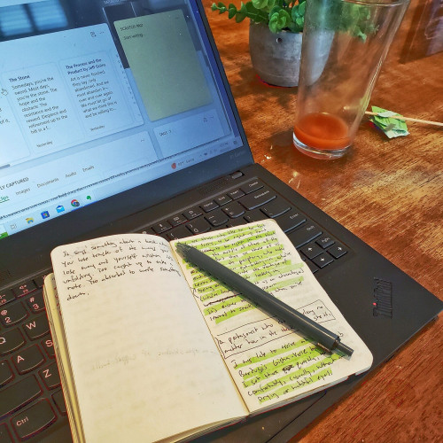 A small pocket notebook sitting on top of a laptop, on a wooden table.