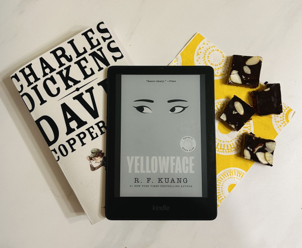The book, David Copperfield by Charles Dickens, Yellowface R. F. Kuang (on my Kindle), & some peanut butter chocolate fudge on a yellow and white napkin.