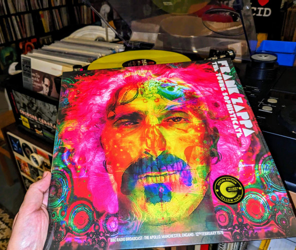 colourful cover of "Frank Zappa - The Young Sophisticate" showing Frank's head with skull features in bright yellow face & pink hair. Yellow vinyl playing in the background.