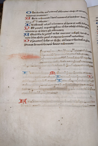 A parchment page with black manuscript text decorated with red and blue initials.
Half down the page, the text is scraped away leaving some visual evidence of the words.