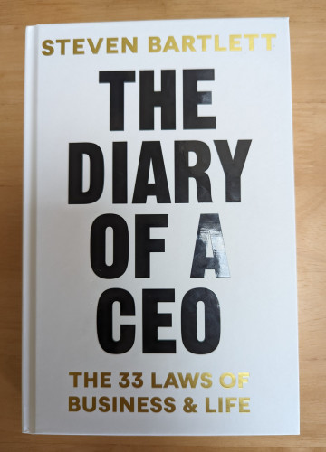 Front cover of "The Diary of a CEO" by Steven Bartlett with the subheading "The 33 Laws of Business & Life". It is a plain white cover with the title in large black letters and the author and subheading in gold. 