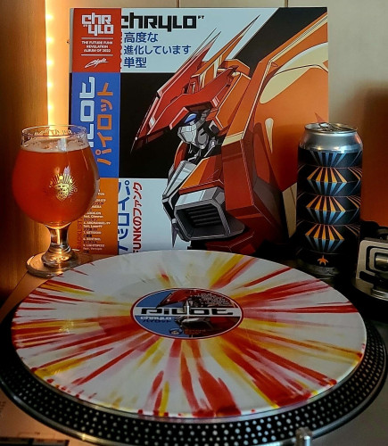 An Orange & White sunburst vinyl record sits on a turntable. Behind the turntable, a vinyl album outer sleeve is displayed. The front cover shows a large top half of a mech (giant robot). An obi strip is on the left. 

To the left of the album cover is a tulip glass filled with beer featuring a hop with a halo and the phases of the moon going around it. On the right of the album cover is 16oz can with blue and orange triangles meeting at the wider end on a black background in multiple rows creating an interesting effect. At the bottom of the can is a small orange starfish. 