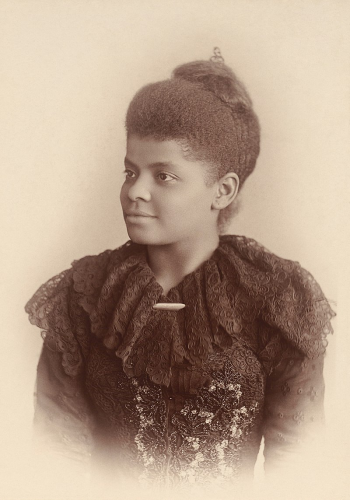 A black and white photograph of Ida B. Wells. She is dressed in a beaded lacy dress and is looking confidently to the viewer's left. 