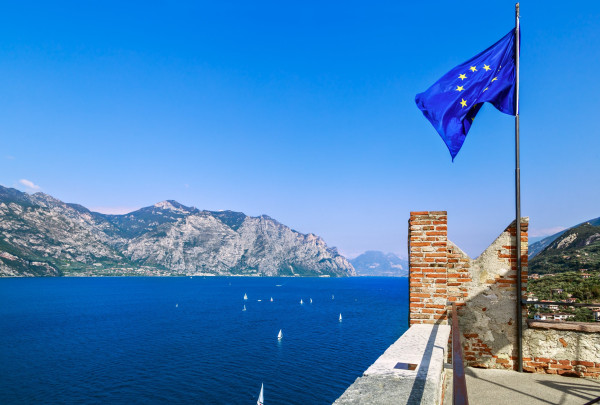 A long-view photo of Lake Garda and the town of Malcesine in Italy, with an EU flag in the foreground.