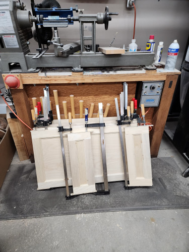Doors and drawers glued up and are in clamps leaning against lathe stand.