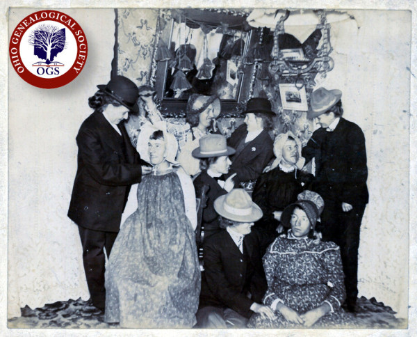 This is a black-and-white photograph of four men and five women. The men are all wearing women's dresses and bonnets and the women are all wearing men's suits and hats. None of the subjects is looking at the camera and they all seem to be smiling.