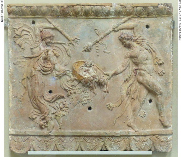 A maenad and a satyr dance, holding a thyrsos and a torch aloft, one hand each on the basket in which lies the vine-crowned baby Dionysos.