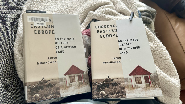 two identical copies of Jacob Mikanowski’s Goodbye, Eastern Europe on a blanket-covered lap. 