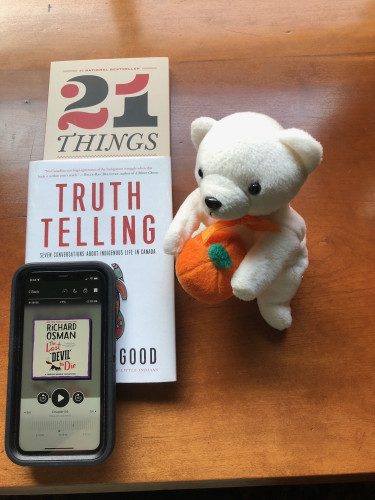 Silent book club member Anne-Louise's recent and current reading, including 21 Things You May Not Know About the Indian Act by Bob Joseph, Truth Telling by Michelle Good and The Last Devil to Die by Richard Osman e-book, accompanied by a white polar bear toy wearing an orange ribbon and holding a plush pumpkin