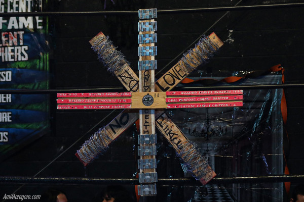 Fan made weapon chaos symbol with 2 crossed barbed wire 2x4s, a carpet strip 2x4, and gusset plate 2x4 suspended on ropes