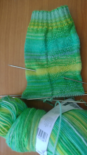 A sock knitting project. The leg of a sock is finshed, it's on the needles and the heel turn will be next. At the bottom of the picture is a ball of yarn to finish the sock.

It's all in several shades of bright green.