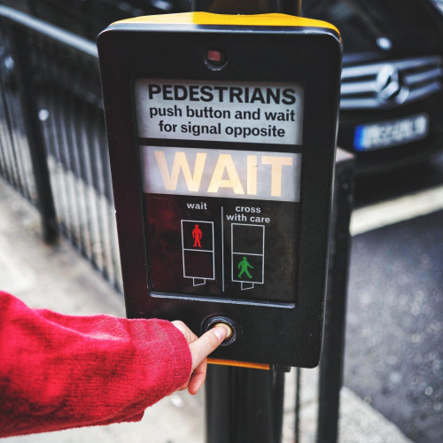 Crosswalk sign, the word "wait" illuminated. A person's hand pressing the button.
