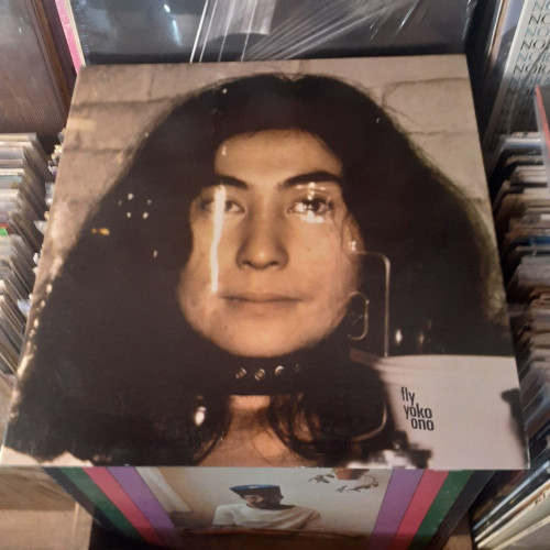 Album cover features a photograph of YO. She is wearing a black leather collar with metal studs.  There is a clear plastic panel in front of her face.  A paper cup is seen to the side. 