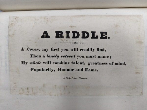 A small leaflet with the tittle "A Riddle", that says:

"A Cover, my first you will readily find,
Then a lonely retreat you must name;
My whole will combine talent, greatness of mind,
Populariy, Honour and Fame" 

At the bottom is the name of the printer: "J. Clark, Printer, Newcastle" 
