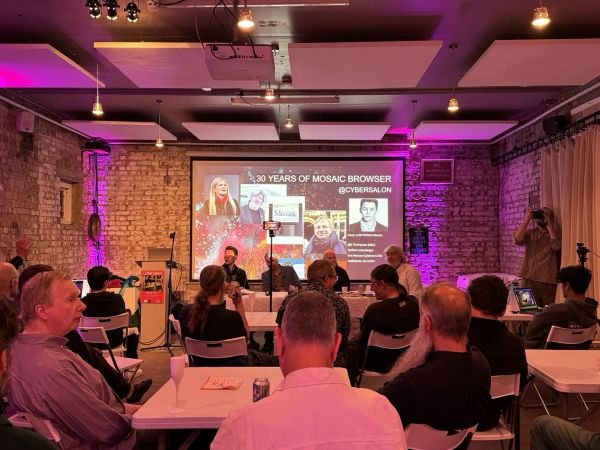 A group of people sitting in a brick-clad room, a panel of individuals at the front with a slide showing "30 years of Mosaic browser @Cybersalon"
