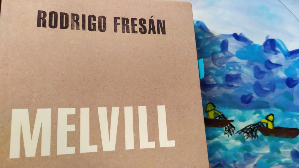 Part de la coberta del llibre Melville de Rodrigo Fresán, darrera el llibre es veu pintat el mar amb 2 pescadors amb xarxes a un plat de ceràmica