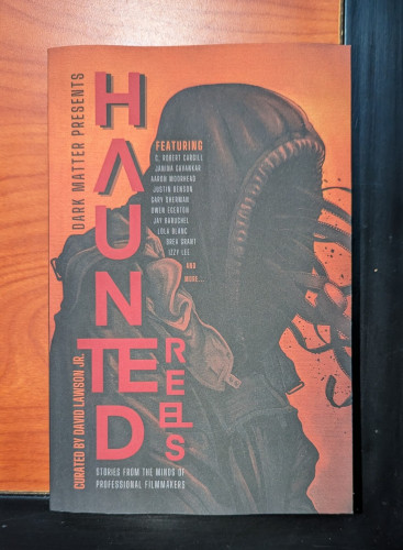 Paperback for the HAUNTED REELS anthology. It has a figure shrouded in black, with film strips streaming out of the darkness where its face should be