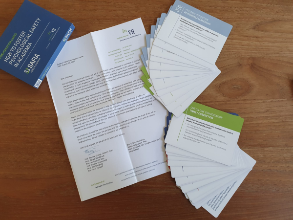 photograph of a letter laying on a table with cards spread out around it. Top left corner a blue box with text "how to foster psychological safety in academia" printed on the box. 