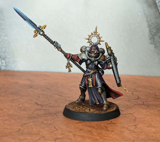 Adepta Sororitas mini with a power spear, painted with silver, gold, and black armor and purple robes with red lining. She finally has a head attached!