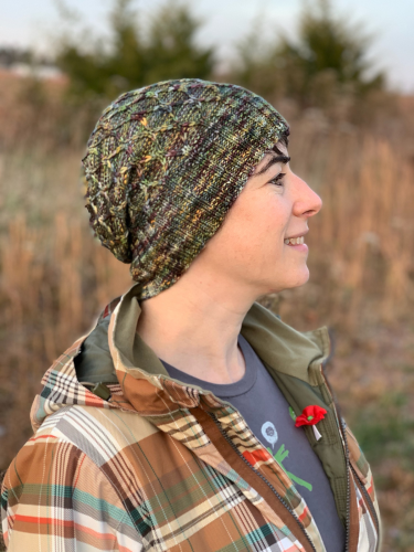 It's me! Seen in profile, modeling the Passing Days hat (a handknit hat in autumnal shades, with a nifty twisty stitch pattern). I am also wearing a plaid jacket with a Remembrance Day poppy tucked into the lapel, and standing in front of golden-brown grasses, which are blurred in the background.