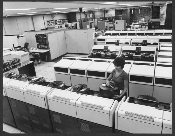 A woman handles a large data-cassette from a seventy's computer. The computing power and memory storage on display here would be shamed by a ten year old mobile phone.

This is the A.C.I. computer office, Melbourne, 1979. Photographer Wolfgang Sievers. 