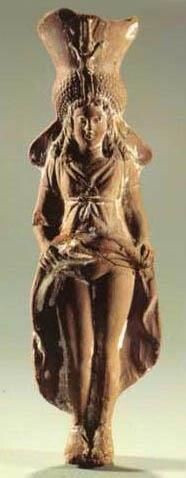 Statuette of a goddess identified as Isis-Aphrodite with a large head-dress reminiscent of a pharaoh's crown. She lifts her dress, baring her pubic triangle.