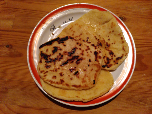 A white plate with a red rim and the words "Bon appetite" filled with three naan breads.