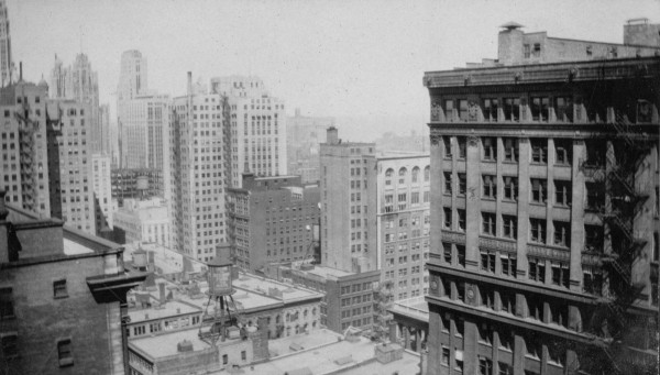 View from far above street level of Chicago from some time in the early 1900s. Large brick and stone high-rises line the frame - below, shorter buildings and a rooftop water tower.