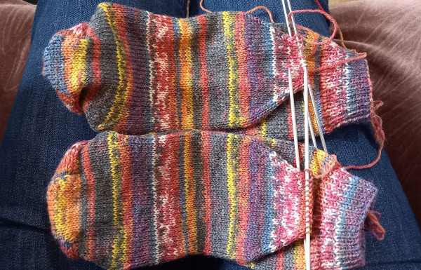 Photo shows a pair of hand knitted socks, sole upmost, ready to have the toes sewn up. The pattern of dye on the yarn very pleasingly matches on both socks.