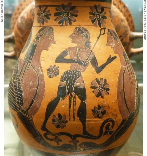 Black-figure vase painting on a wine jug depicting a youthful Hermes, beardless and with long hair. He is holding his kerykeion staff and is standing between two sphinxes. Flowers decorate the vase all around them.