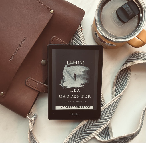 My purse laying on its side, my Kindle featuring Ilium by Lea Carpenter, & my yellow coffee mug filled to the brim with coffee. 