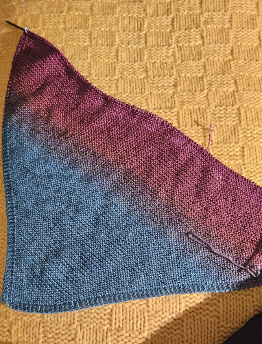 knitting in progress. lap blanket knit diagonally. color ranges from blue to red.