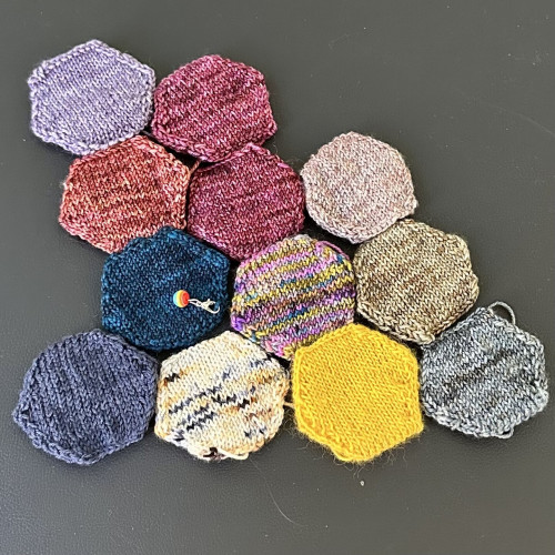 12 knitted hexagons of various colors displayed next to each other but unconnected