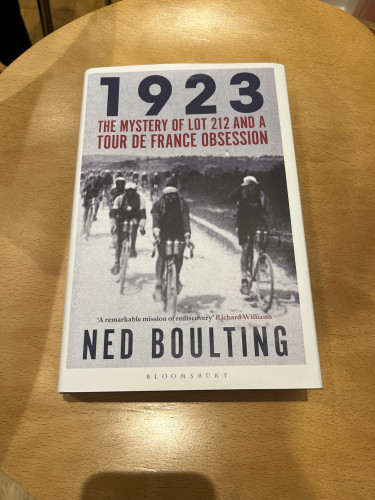 The cover of 1923 by Ned Boulting. Depicts a scene from a newsreel from the time of a group of men riding in the Tour de France.