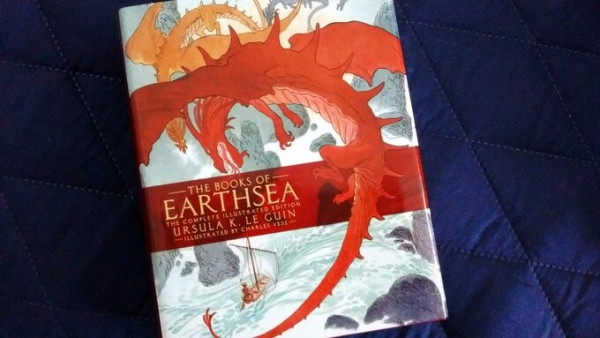 This is the cover for the special collection, containing all of The Books of Earthsea, by Ursula K. Le Guin.
The cover shows a small sailing boat, navigating a stretch of rough sea that is peppered with jagged and dangerously-looking rocks, while above two dragons, one red one orange, seem ready to attack.
The illustration, by Charles Vess, contrast the cool tones of the sea -greens, grays, whites- with the warm tones of the dragons to help guide our sight from the enormity of the beast to the vulnerability of the tiny human figure on the boat.